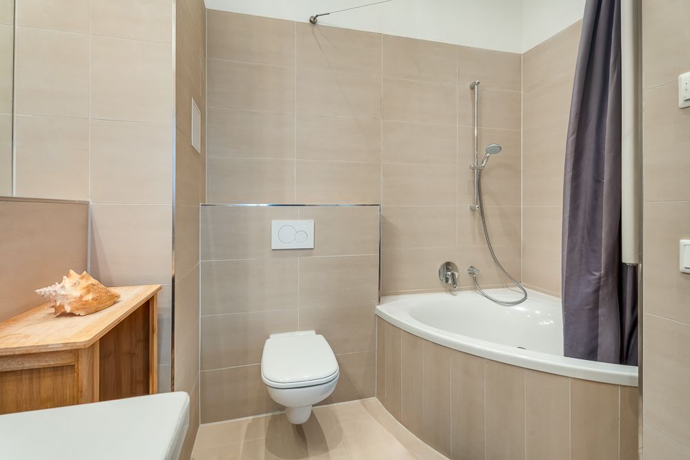 Modernes Badezimmer mit Eckbadewanne, Wandtoilette und Holztisch mit Muschel.
