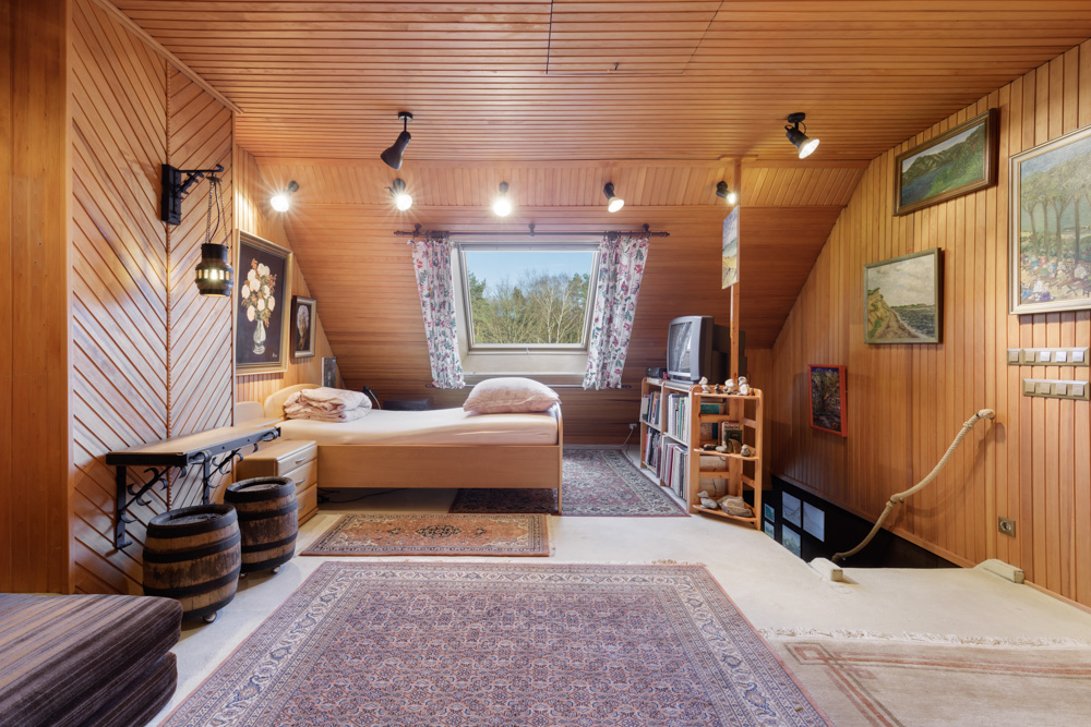 Gemütliches Zimmer mit Holzwänden, Bett, Teppich, Fenster und mehreren Gemälden.