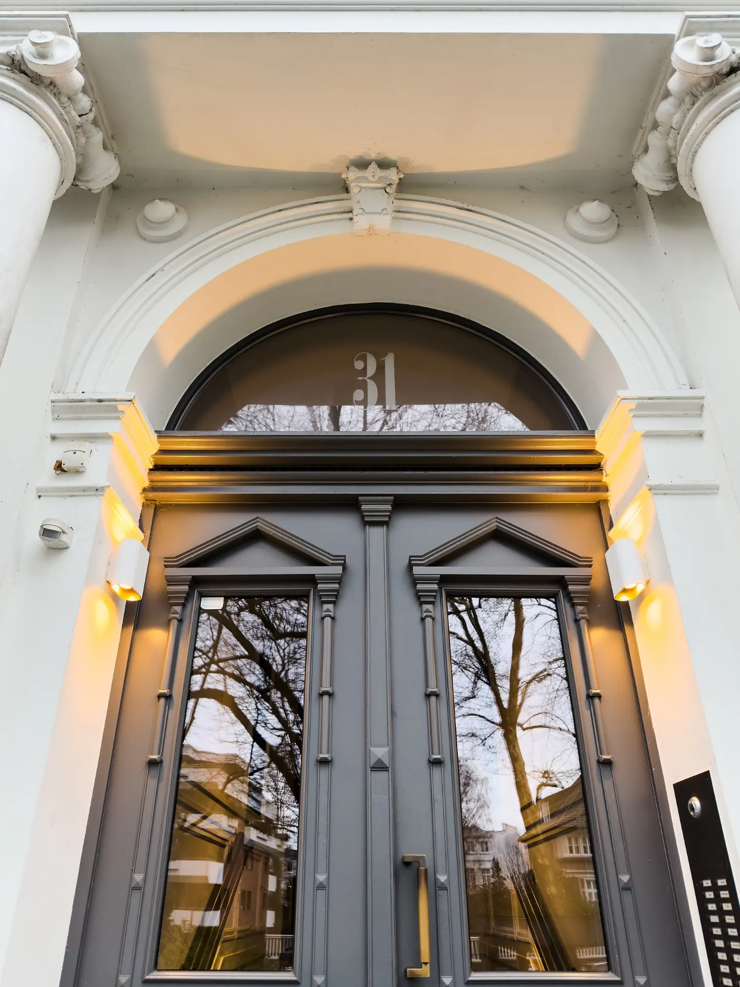 Graue Eingangstür mit Glas und Hausnummer 31, umgeben von weißem Mauerwerk.