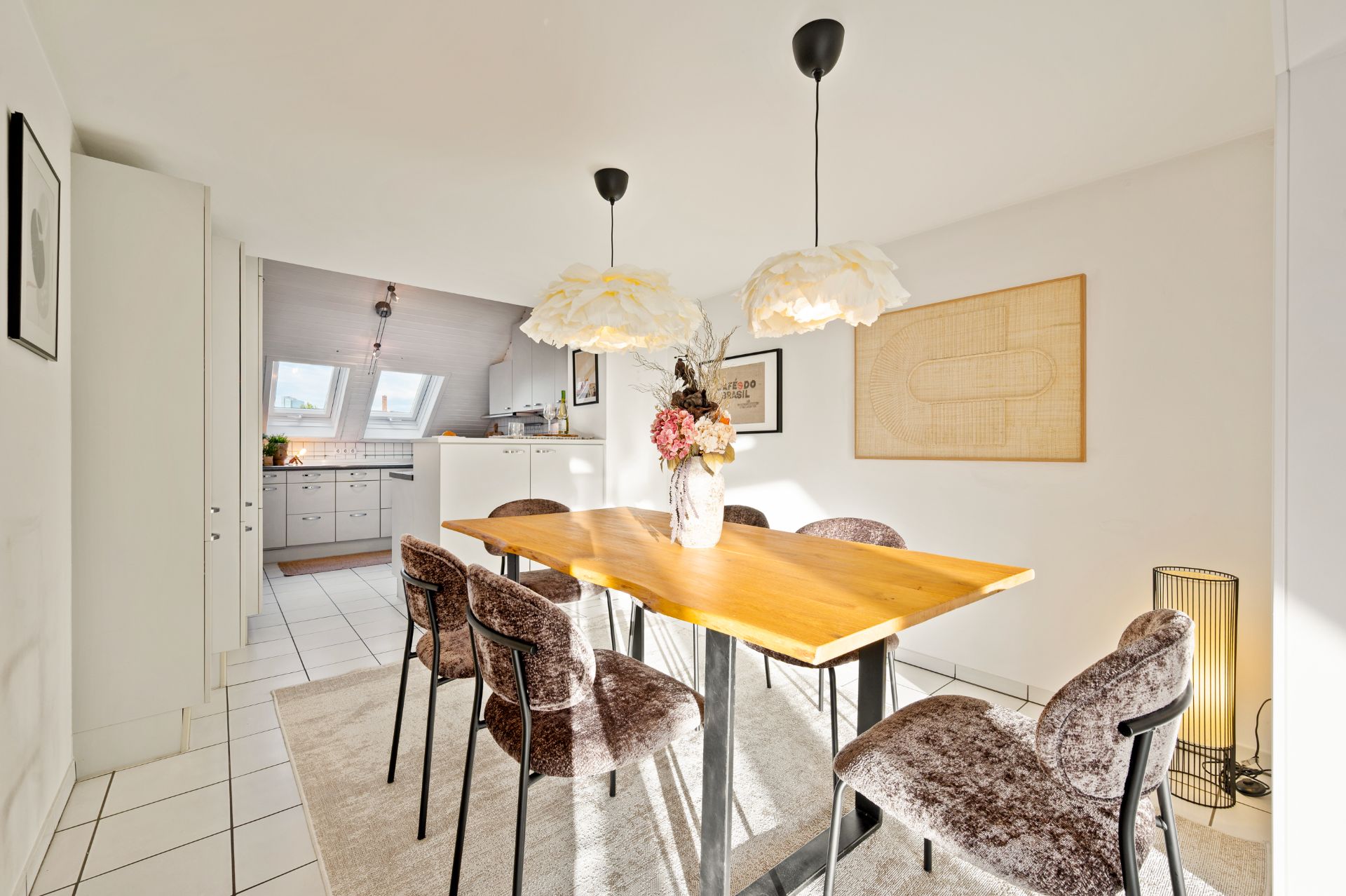 Esszimmer mit Holztisch, sechs Stühlen, Blumenstrauß und Blick in eine helle Küche.