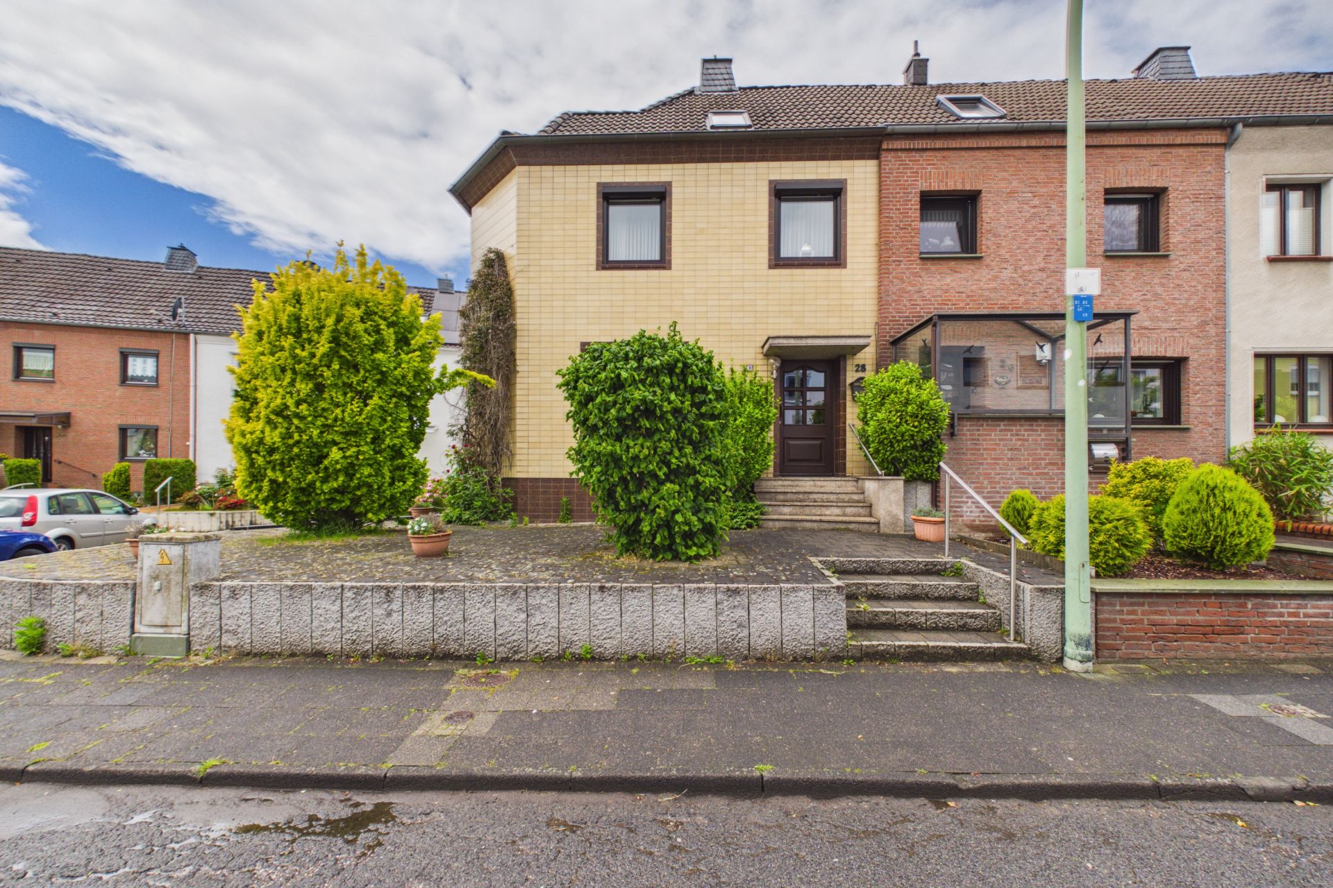 Zweistöckiges Reihenhaus mit Vorgarten, Sträuchern und Treppen zur Eingangstür.