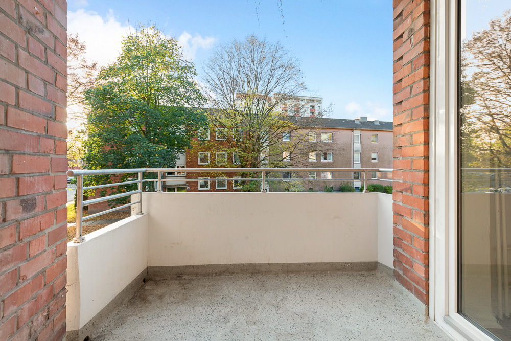 Blick von einem Balkon mit Geländer auf Bäume und ein gegenüberliegendes Wohngebäude.