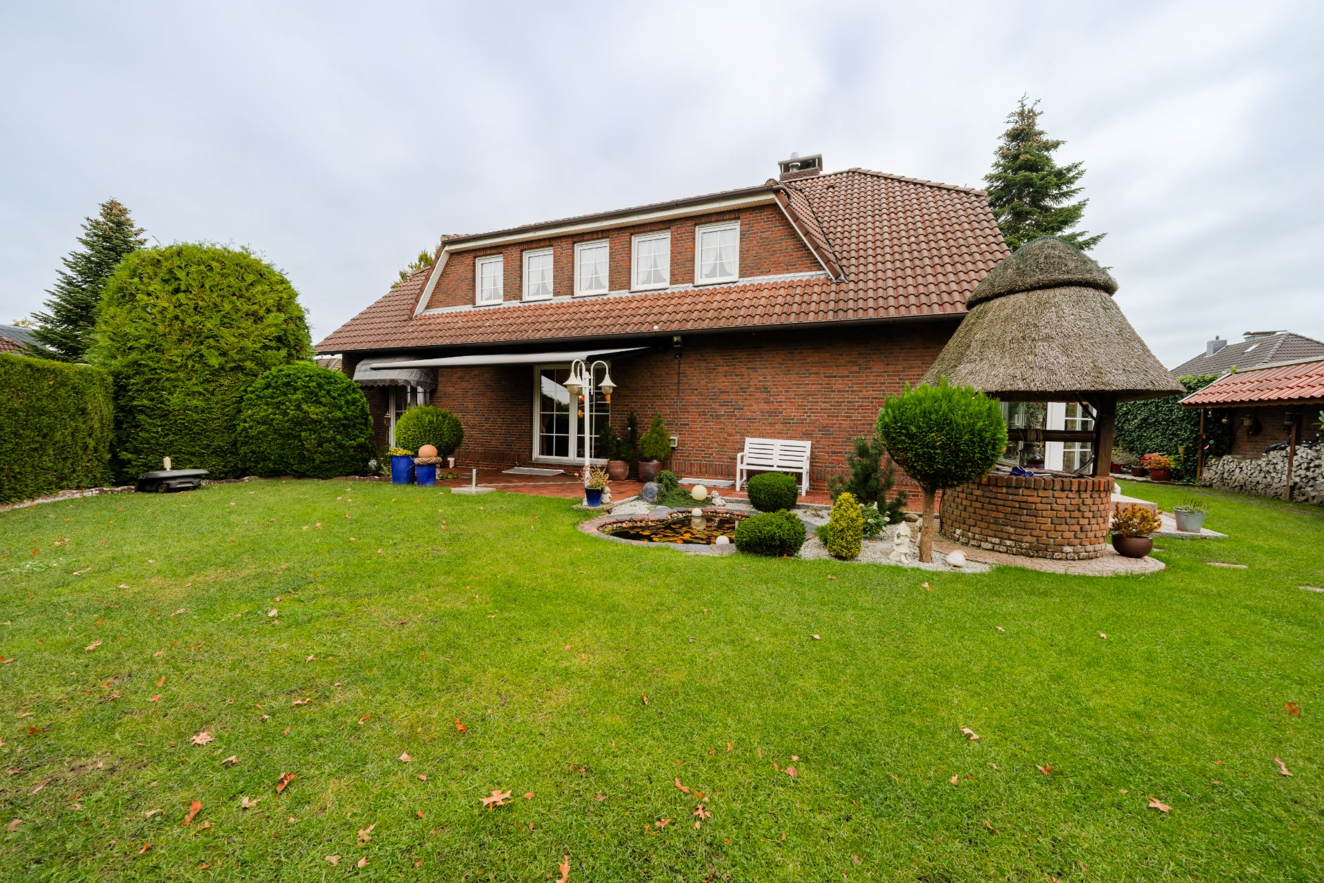 Backsteinwohnhaus mit Garten, Teich und gemauertem Pavillon mit Reetdach.