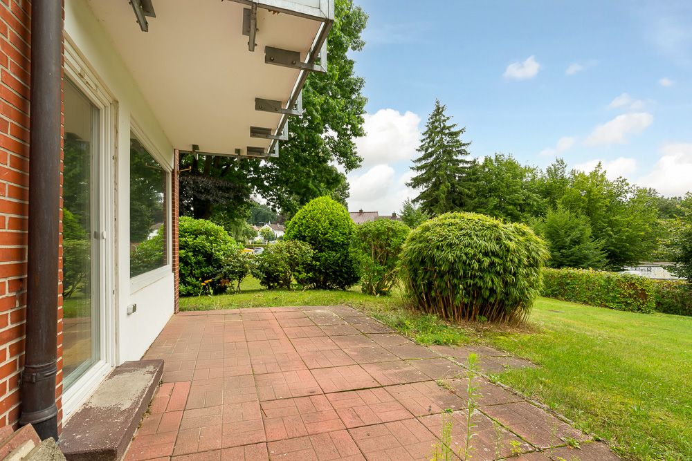 Terrasse mit roten Fliesen und Garten, umgeben von Büschen und Bäumen.