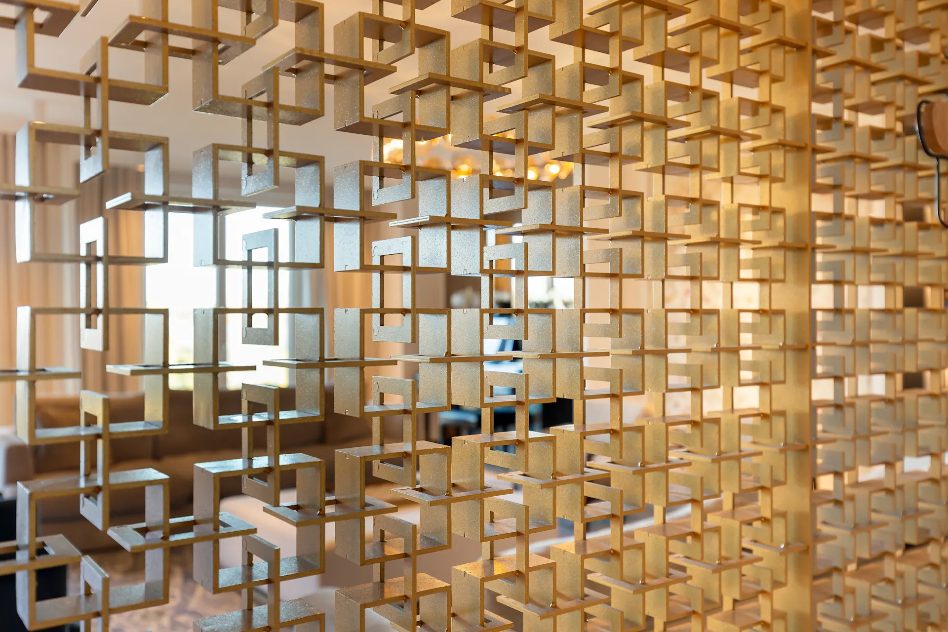 Raumteiler aus goldenen, quadratischen Metallrahmen in einem hellen Wohnzimmer.