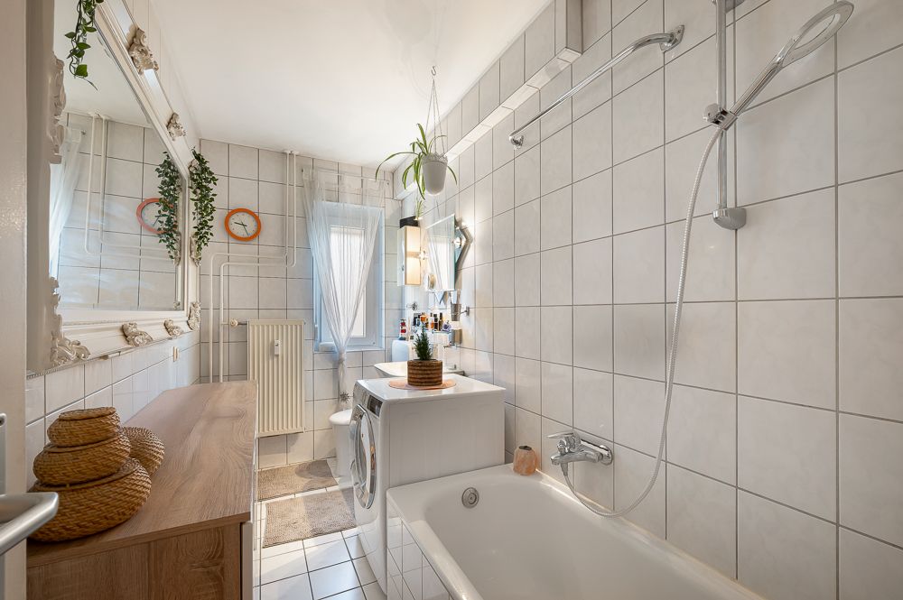 Helles Badezimmer mit Badewanne, Waschmaschine, Spiegel und gefliesten Wänden.
