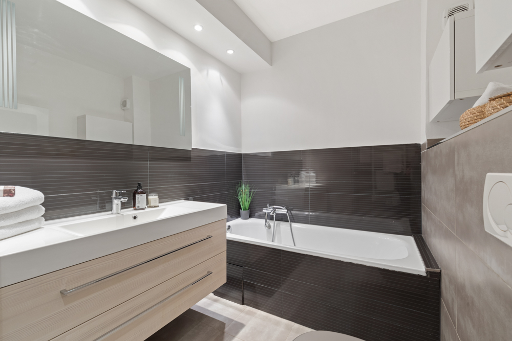 Modernes Badezimmer mit Badewanne, Waschbecken, Spiegel und schwarzer Wandfliese.