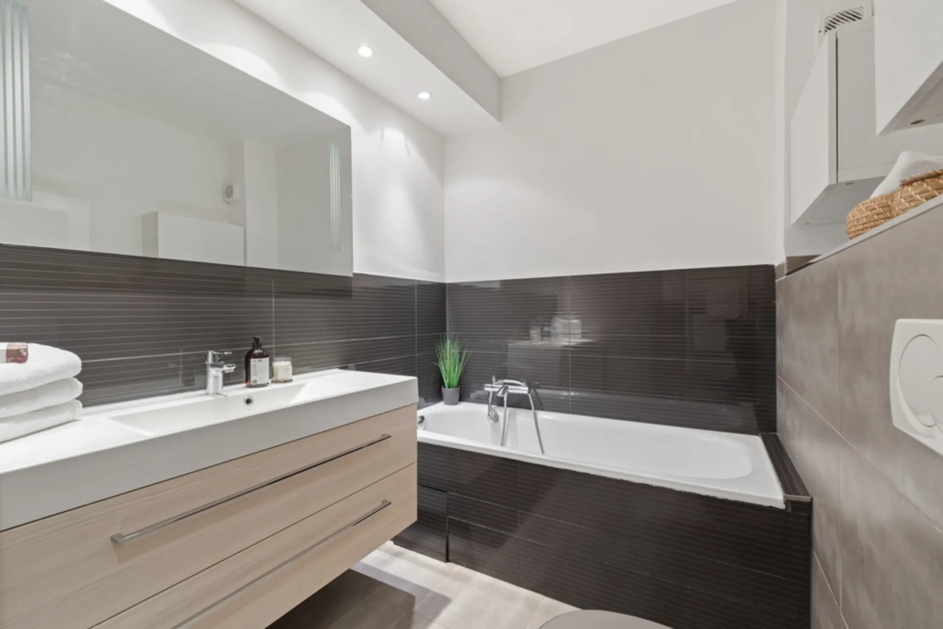 Modernes Badezimmer mit Badewanne, Waschbecken, Spiegel und schwarzer Wandfliese.