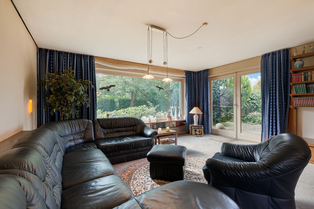 Wohnzimmer mit schwarzem Ledersofa, großem Fenster, blauem Vorhang und Blick in den Garten.