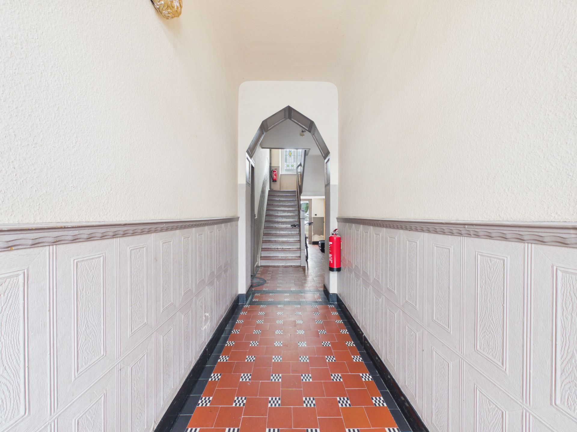 Heller Flur mit gemustertem Boden, Holzvertäfelung und Treppe am Ende.