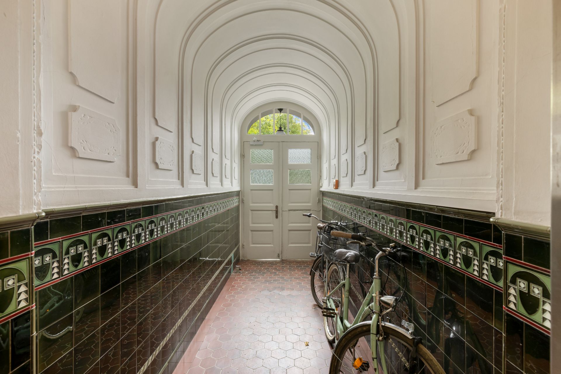 Heller Flur mit weißen Wänden, Fliesen, gewölbter Decke und zwei Fahrrädern an der Seite.