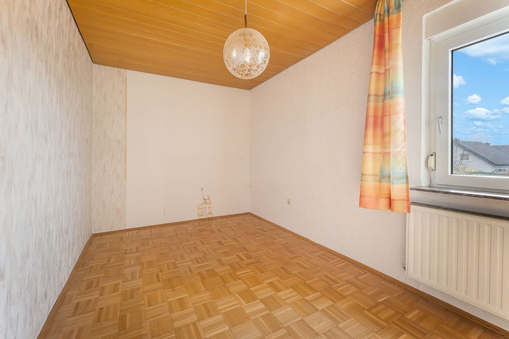 Leeres Zimmer mit Parkettboden, Holzdecke, Fenster und bunter Gardine.