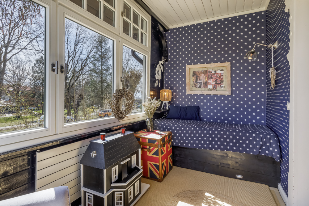 Gemütliche Sitzecke mit Sternentapete, großem Fenster, Puppenhaus und Truhe im Zimmer.