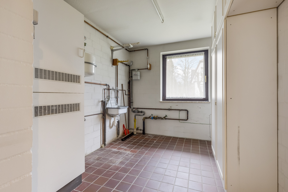 Heller Hauswirtschaftsraum mit Fliesenboden, Wandarmaturen und Fenster.