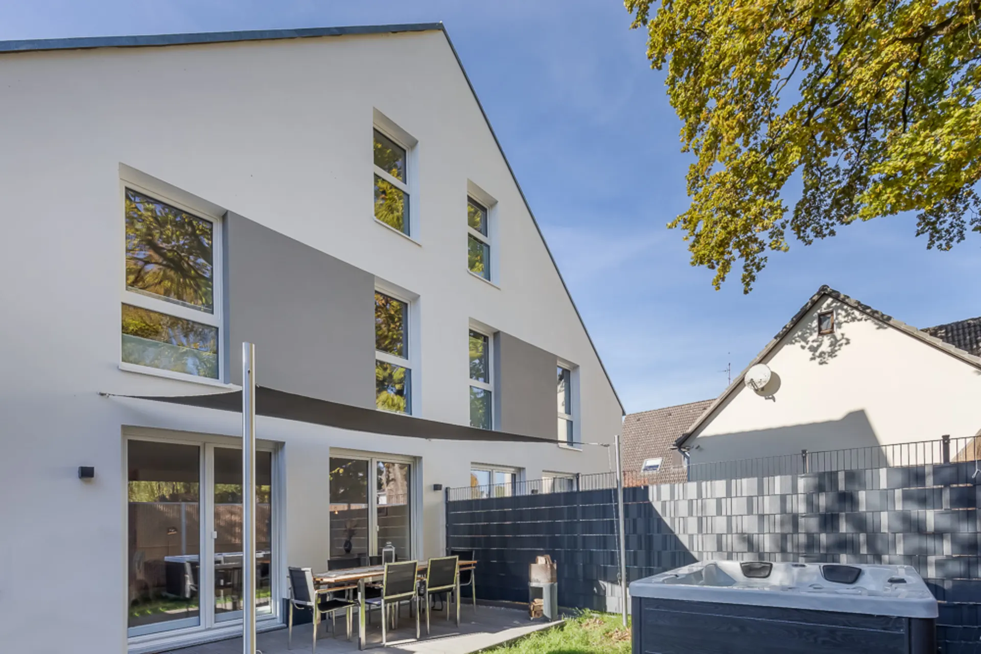Moderne weiße Wohnhausfassade mit Terrasse, Gartenmöbeln und Whirlpool im Garten.