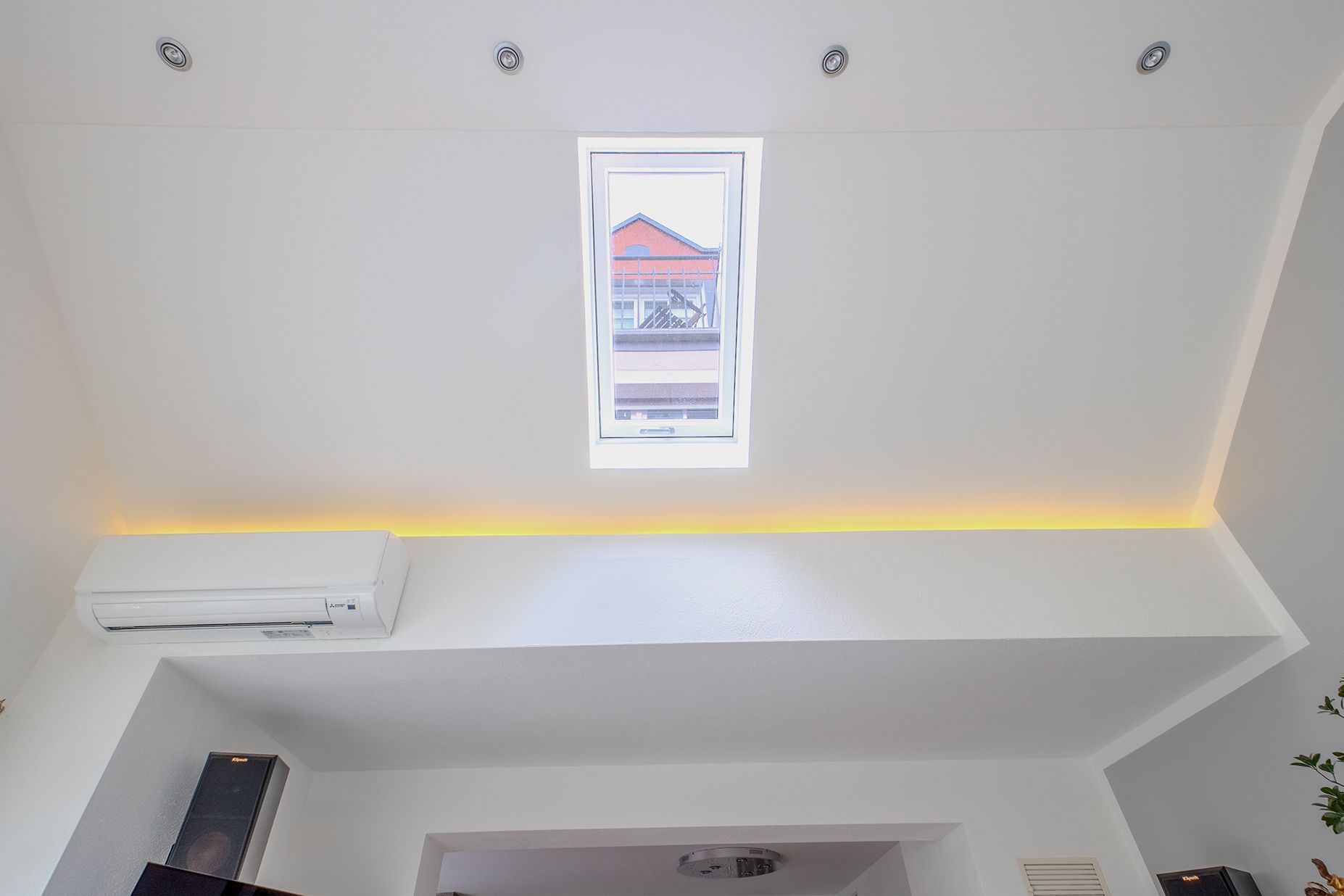 Helles Zimmer mit schräger Decke, Dachfenster und Klimaanlage an der Wand.