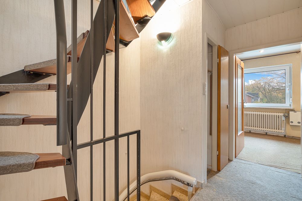 Treppe mit Metallgeländer in einem Flur, daneben offene Tür zu einem Zimmer mit Fenster.