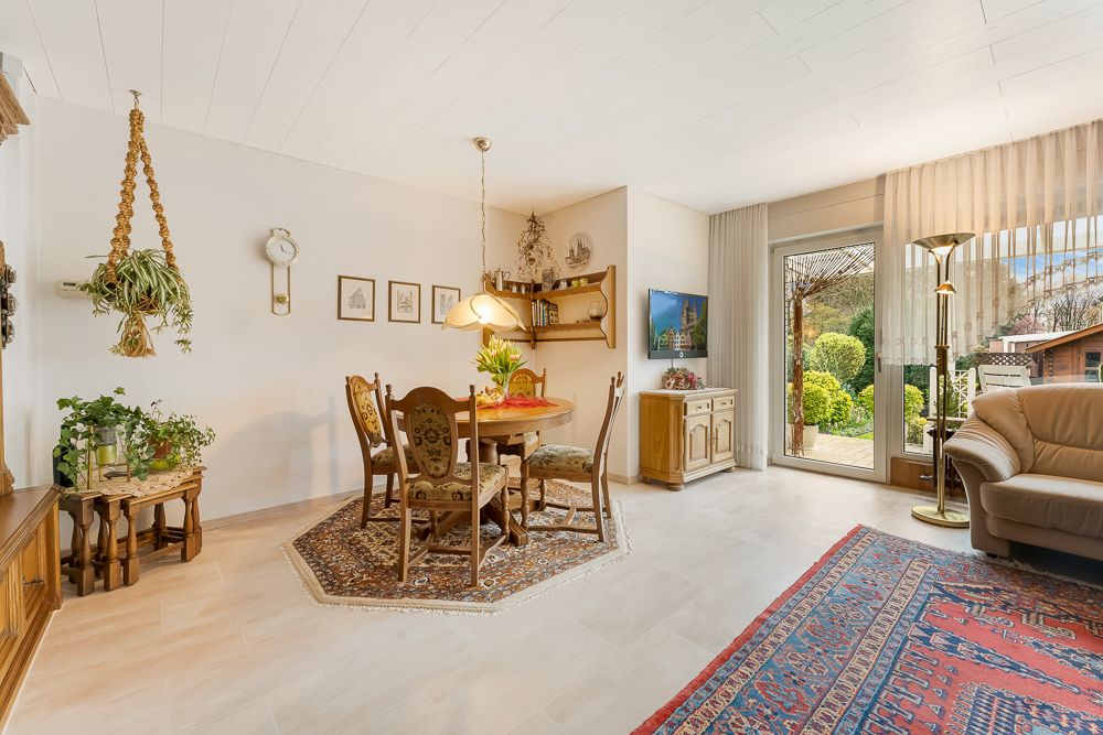 Helles Wohnzimmer mit Esstisch, Teppichen, Pflanzen, Sofa und Zugang zum Garten.