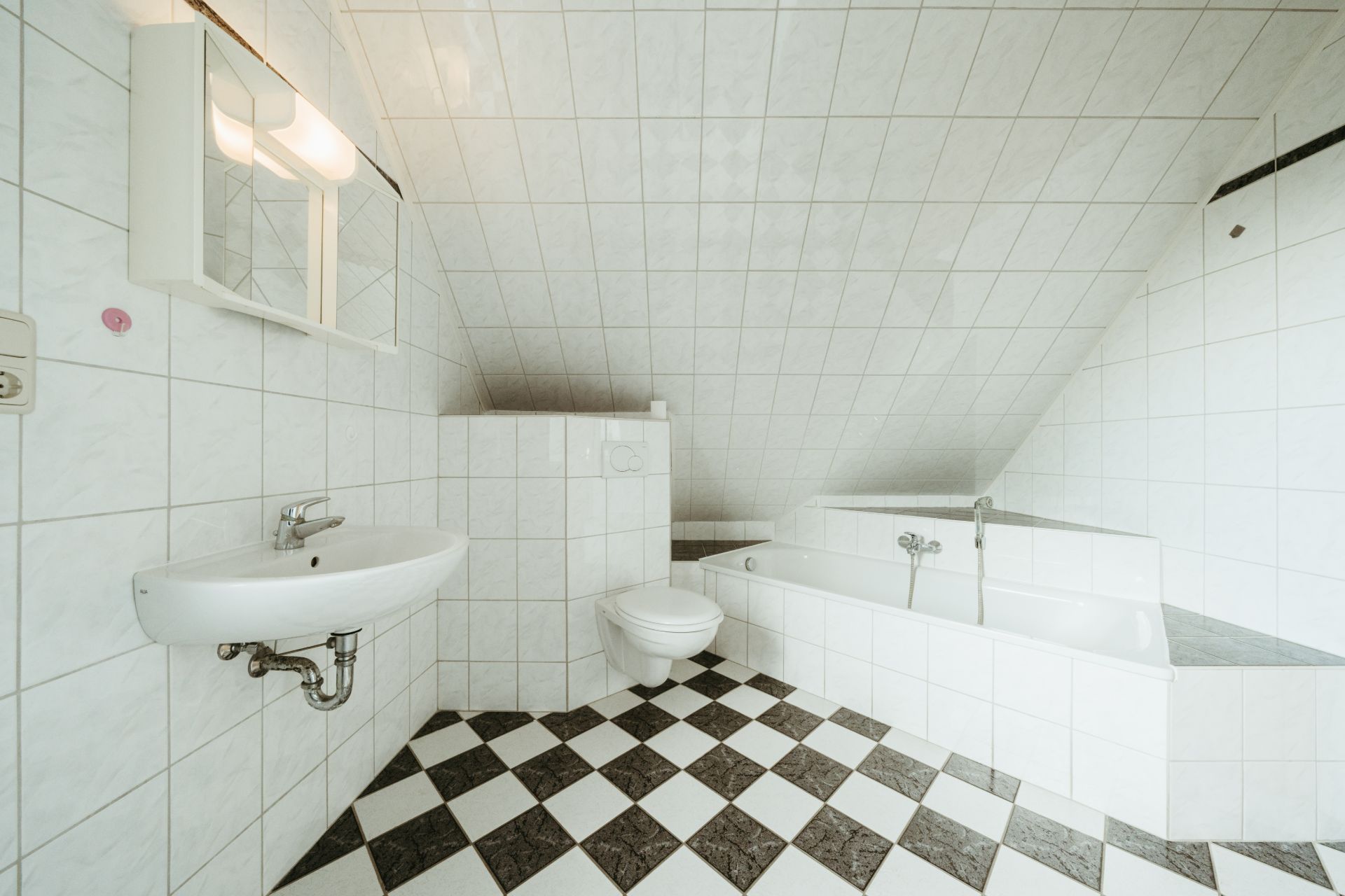 Modernes Bad mit Waschbecken, WC, Badewanne und schwarz-weiß kariertem Boden.