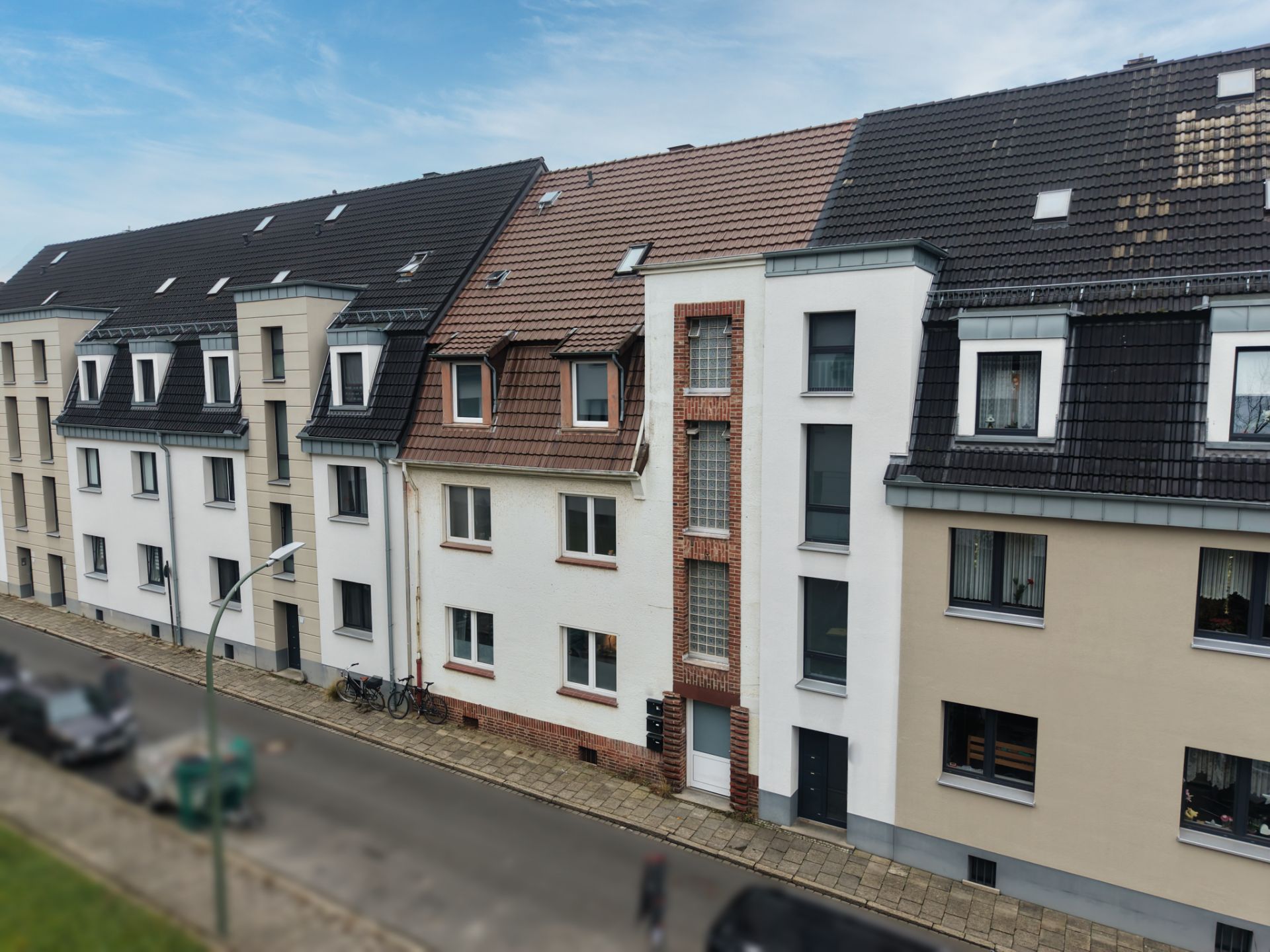 Mehrstöckige Wohnhäuser mit Satteldächern an einer ruhigen Straße.