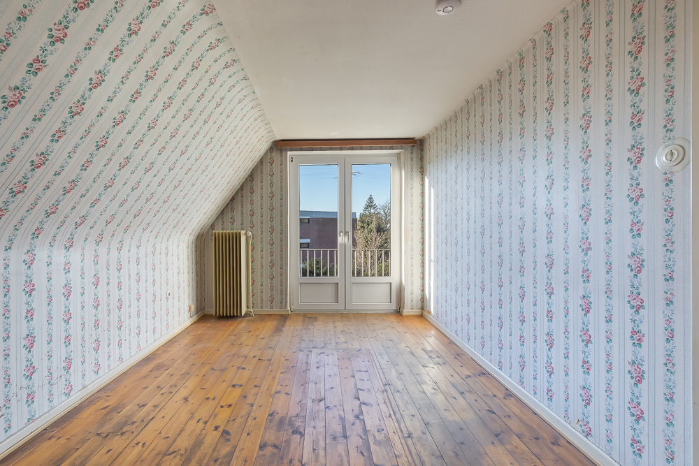 Leeres Zimmer mit Blumenmuster-Tapete, Holzboden und Doppeltür zu einem Balkon.