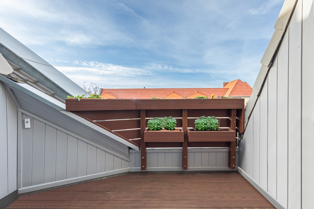 Kleine Dachterrasse mit Holzgeländer und Blumenkästen, umgeben von weißen Wänden.