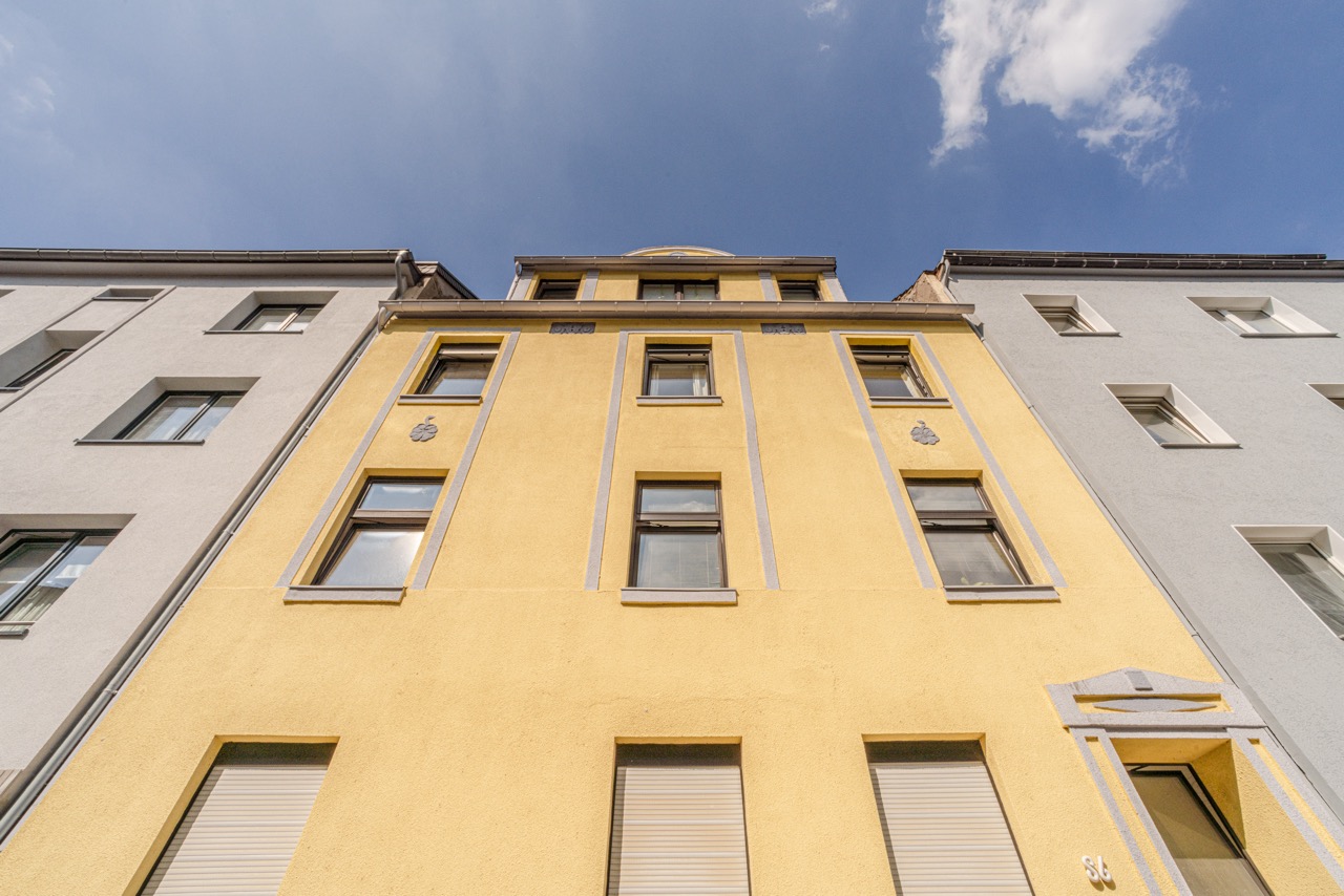 Fassade eines gelben Mehrfamilienhauses mit mehreren Fenstern, von unten fotografiert.