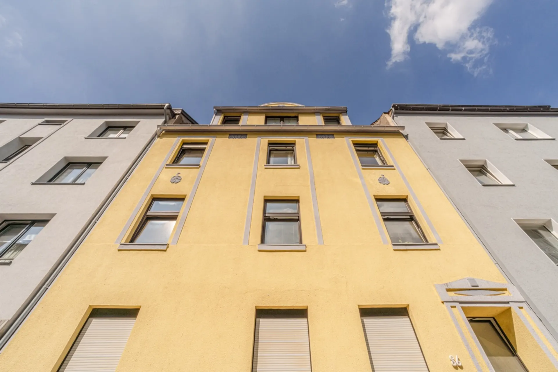 Fassade eines gelben Mehrfamilienhauses mit mehreren Fenstern, von unten fotografiert.