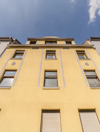 Fassade eines gelben Mehrfamilienhauses mit mehreren Fenstern, von unten fotografiert.