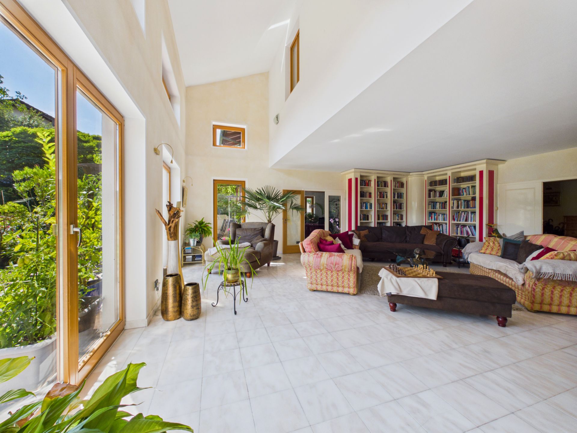 Großes, helles Wohnzimmer mit Sofas, Sesseln, Bücherregalen und vielen Pflanzen.