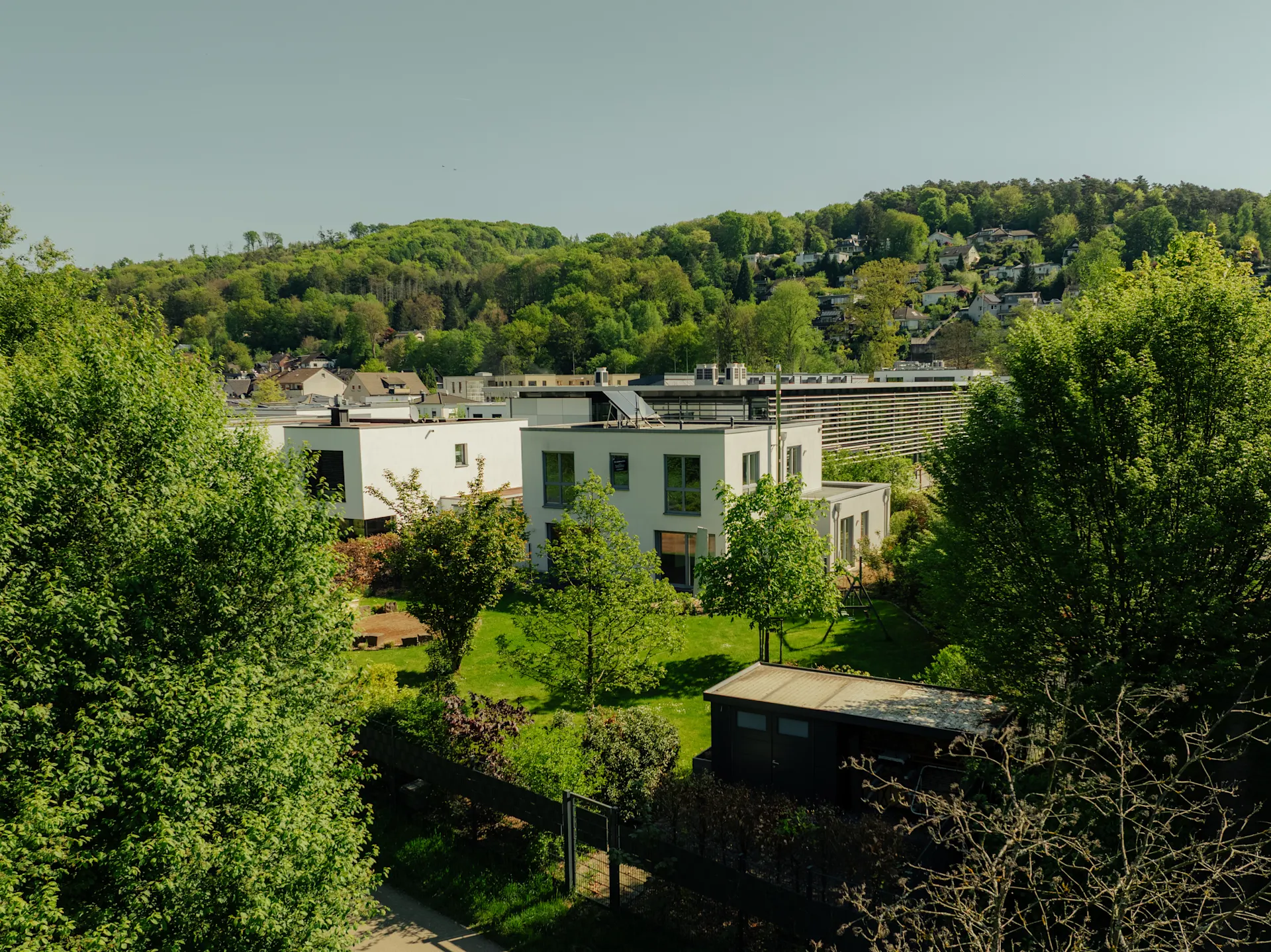 Modernes Wohnhaus mit Garten, umgeben von Bäumen und Hügeln im Hintergrund.