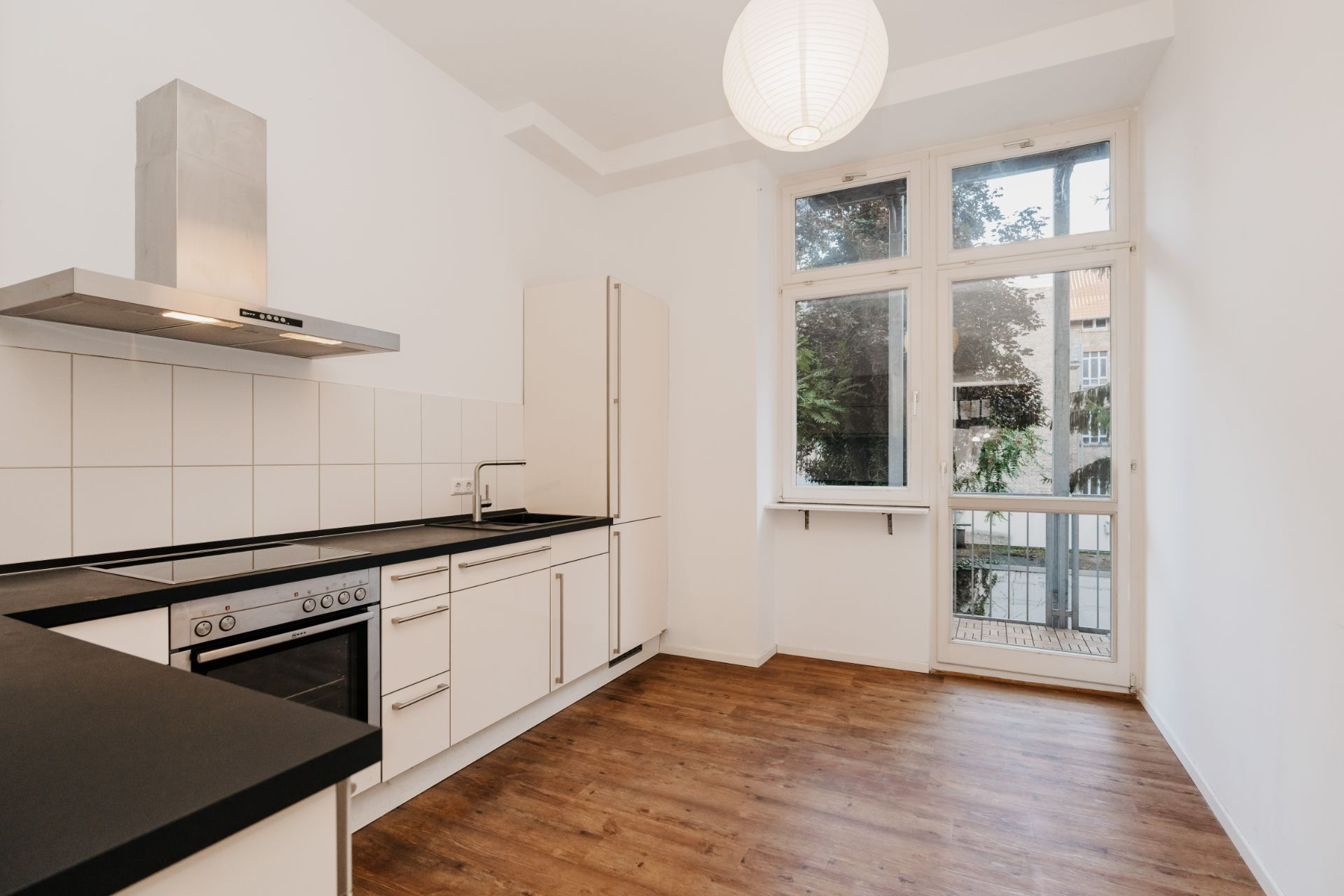 Moderne Küche mit weißen Schränken, Holzfußboden und großem Fenster mit Tür zum Balkon.