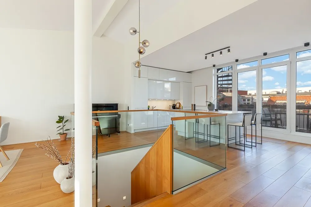 Moderne Wohnküche mit großem Fenster, Holzfußboden und Treppe mit Glasgeländer.