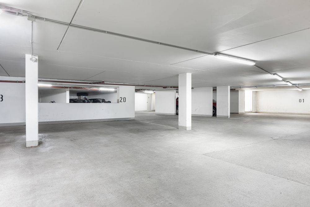 Helle, leere Tiefgarage mit nummerierten Stellplätzen und weißen Wänden.