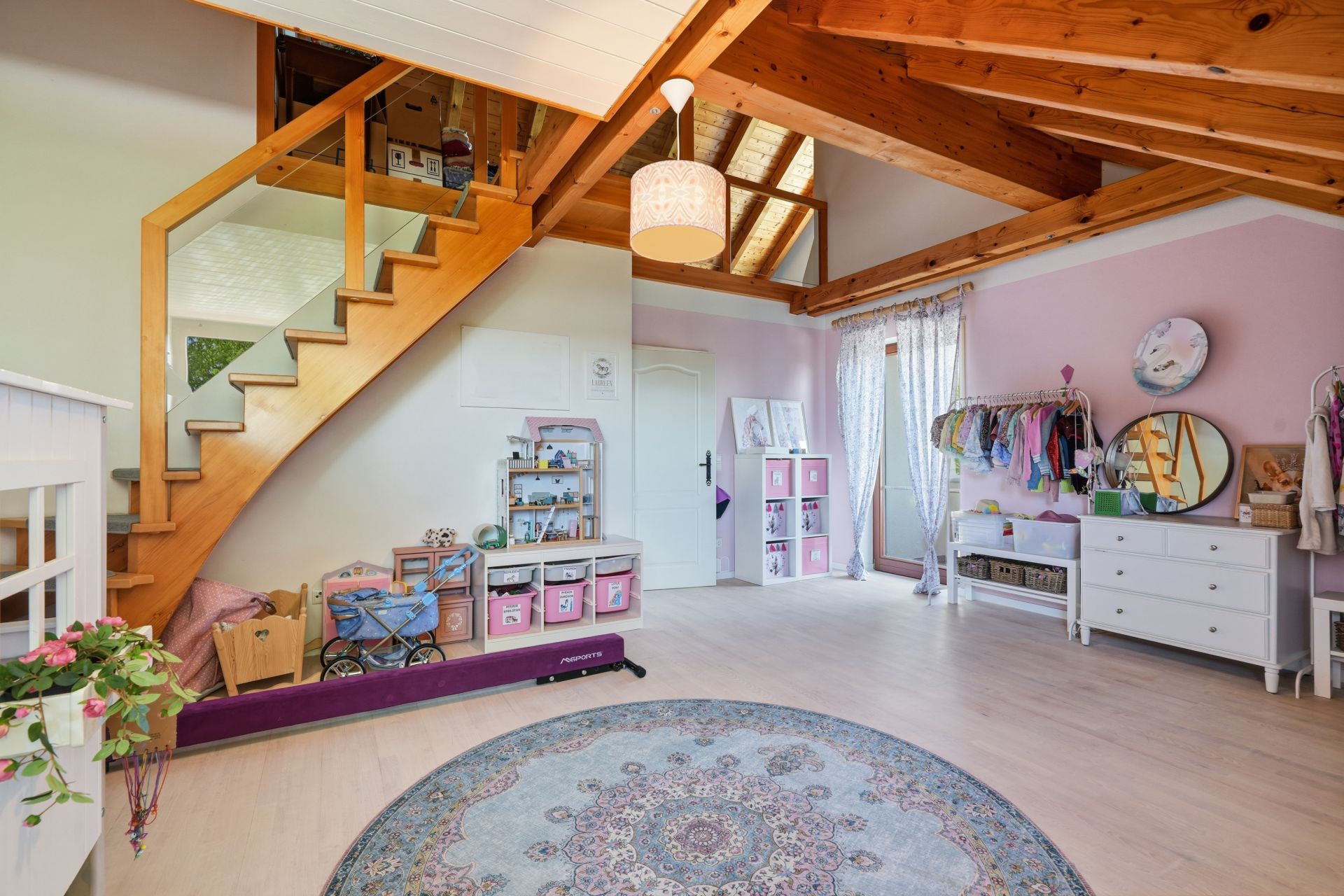 Helles Kinderzimmer mit Holztreppe, Spielzeugregalen, Teppich und sichtbaren Holzbalken.