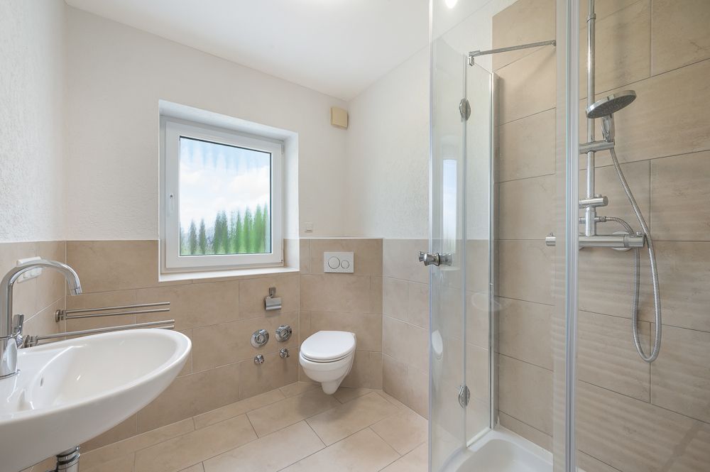 Modernes Badezimmer mit Dusche, WC, Waschbecken und Fenster.