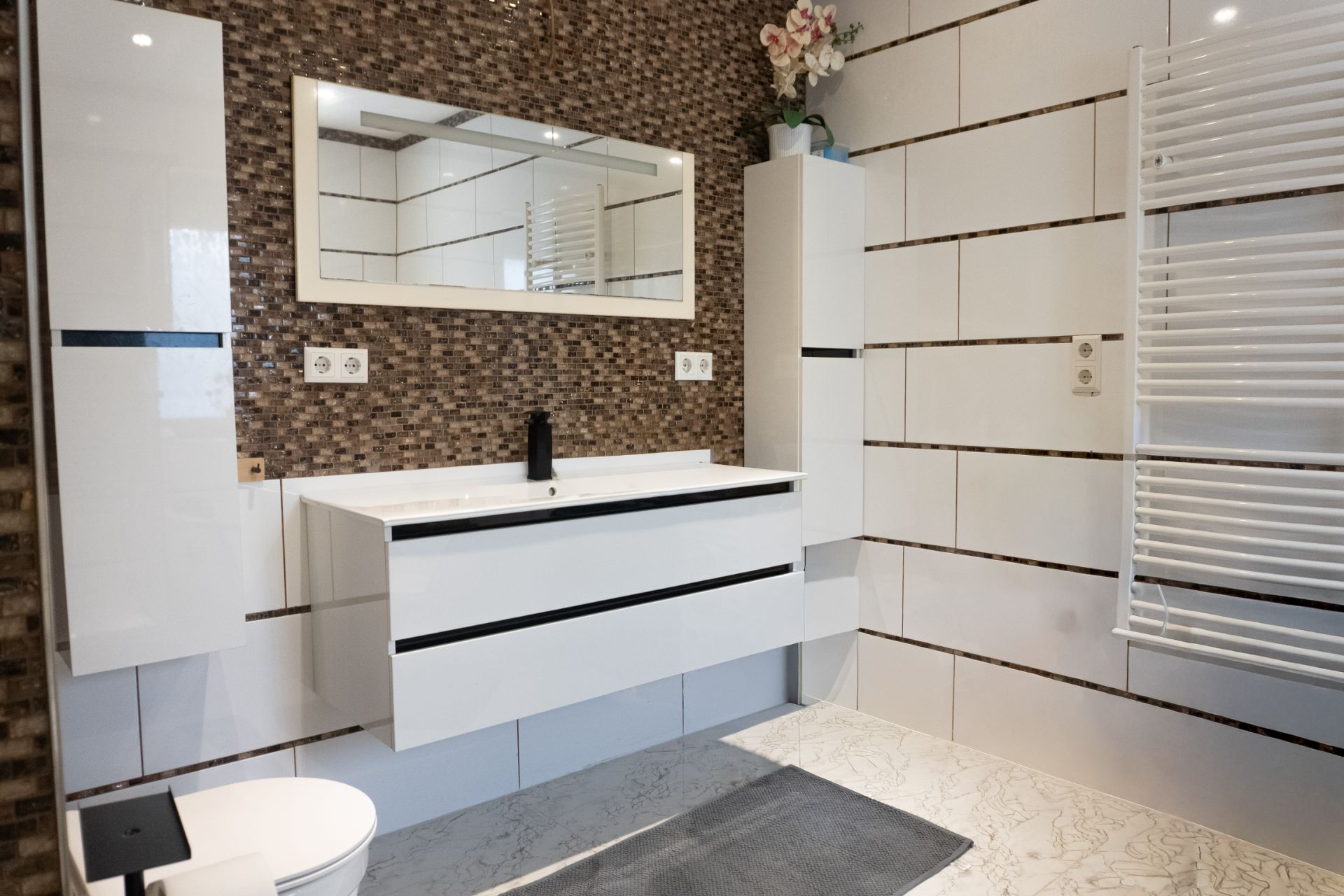 Modernes Badezimmer mit weißem Waschbecken, großem Spiegel und Handtuchheizkörper.