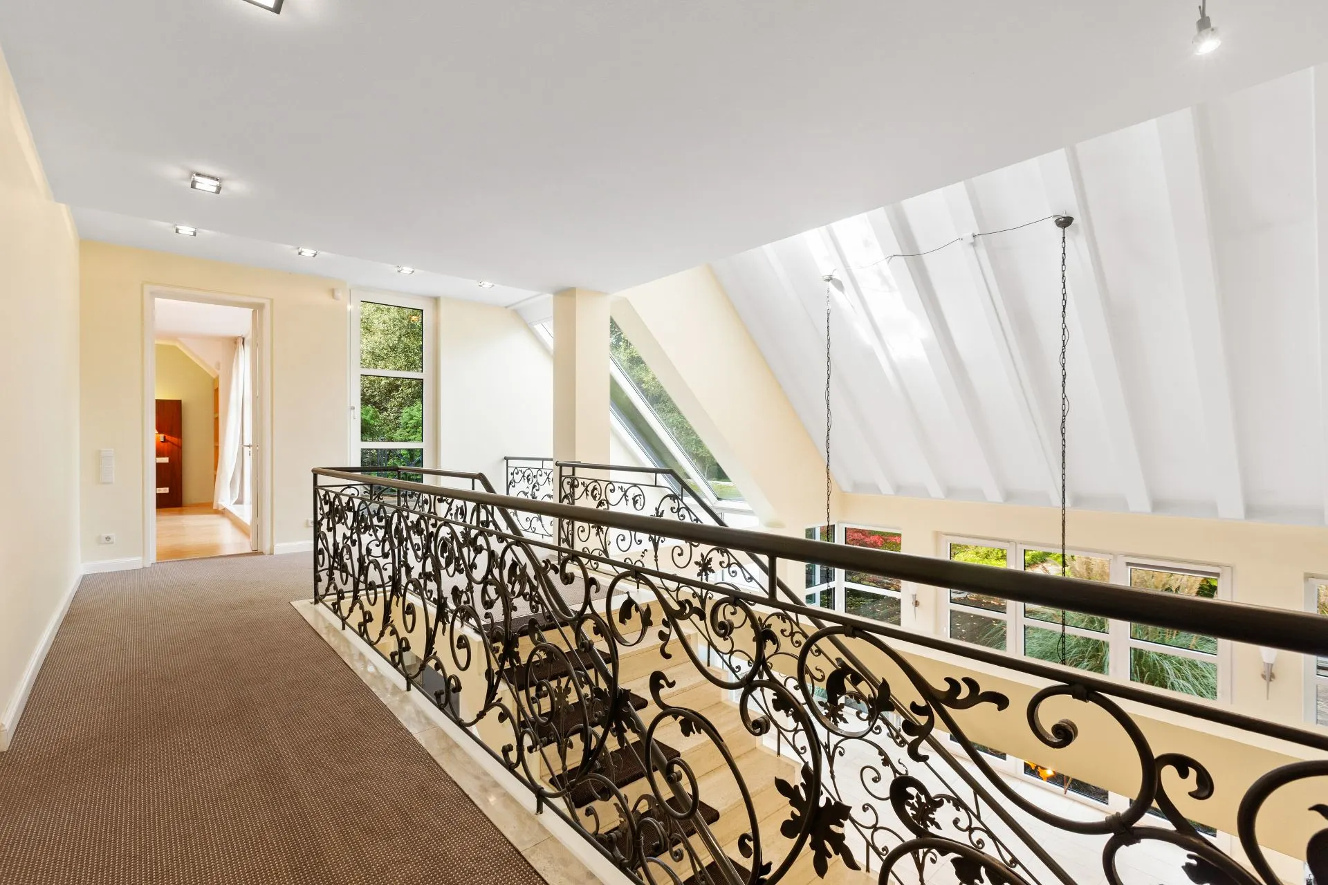 Galerie mit verziertem Treppengeländer, großem Fenster und Blick auf Wohnbereich.
