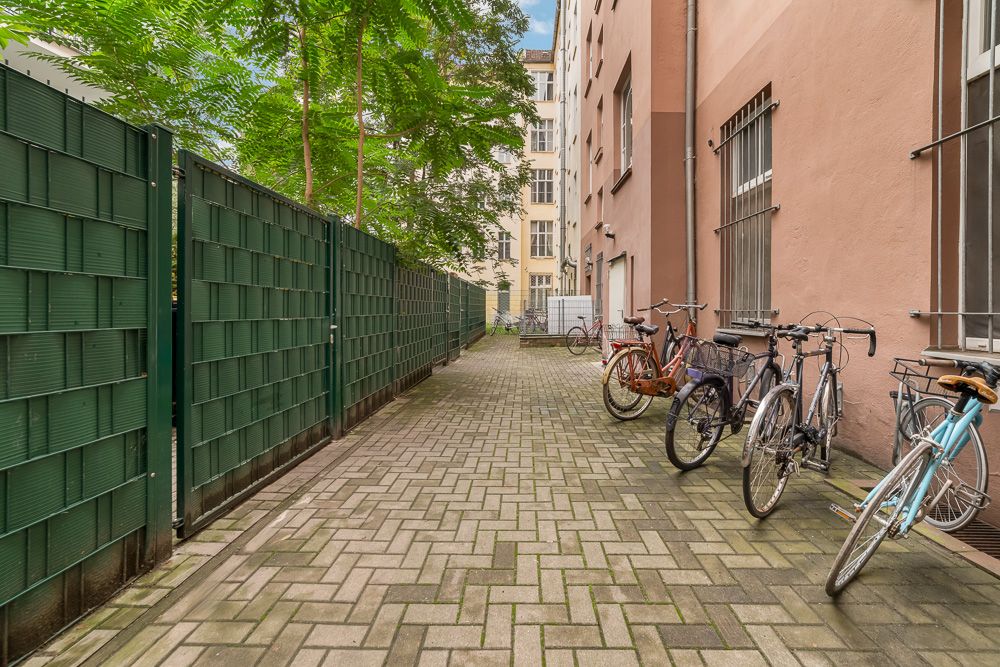 Gepflasterter Hof mit mehreren Fahrrädern an einem Zaun und Bäumen im Hintergrund.
