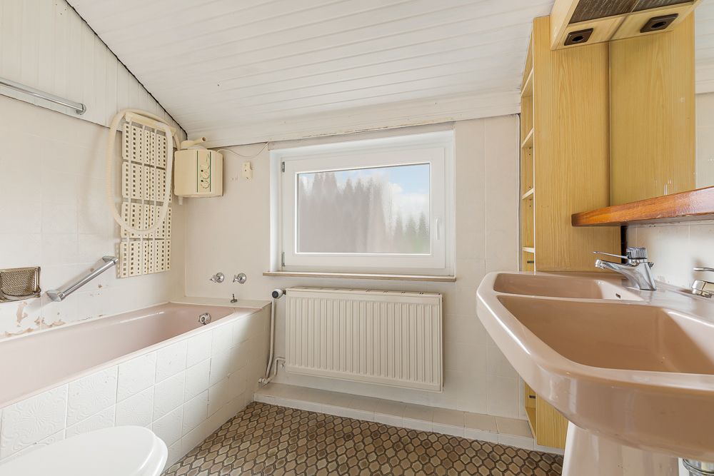 Helles Badezimmer mit rosa Badewanne, Waschbecken, Fenster und Holzregalen.