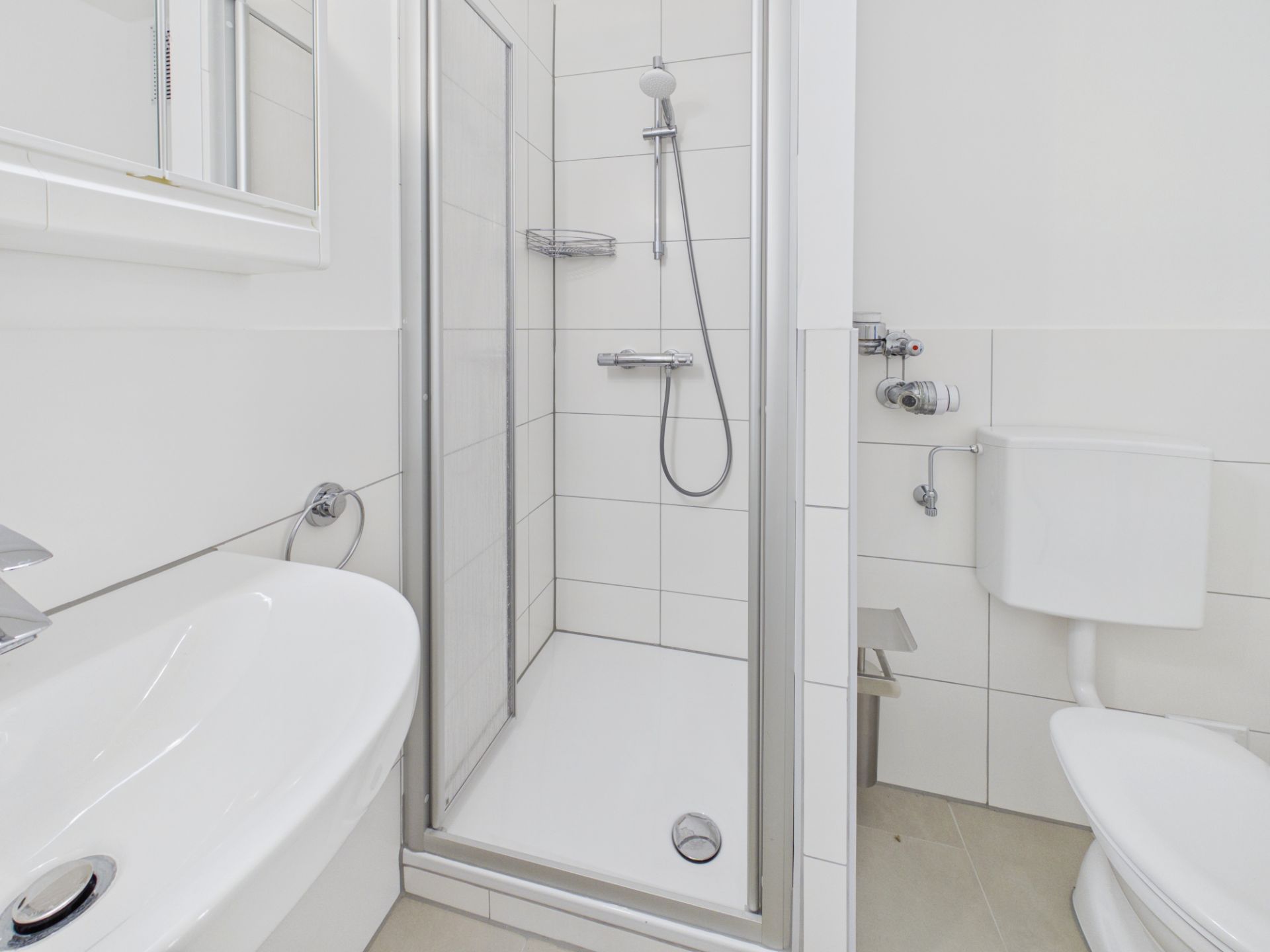 Helles Bad mit Dusche, WC und Waschbecken, weiß gefliest.