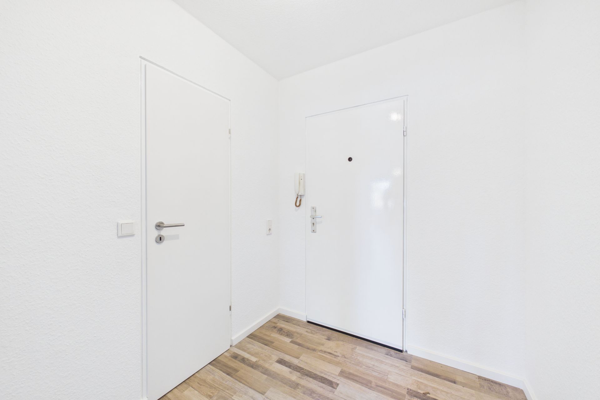Heller Flur mit zwei weißen Türen und Holzfußboden.