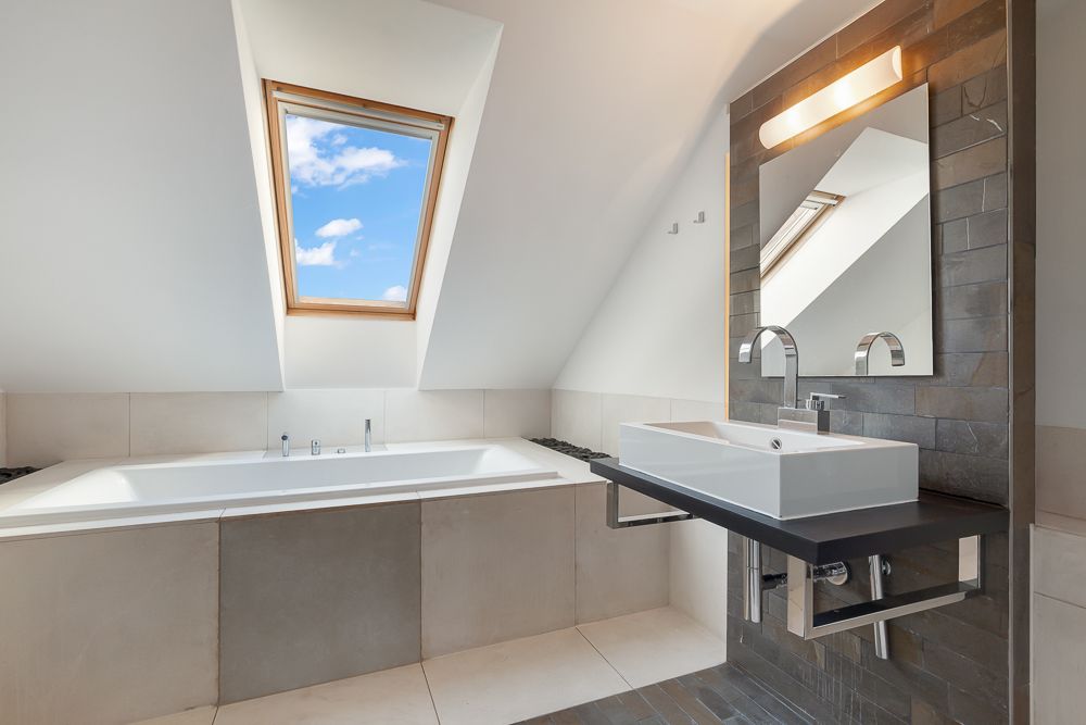 Modernes Badezimmer mit Badewanne, Dachfenster und Waschbecken mit Spiegel.