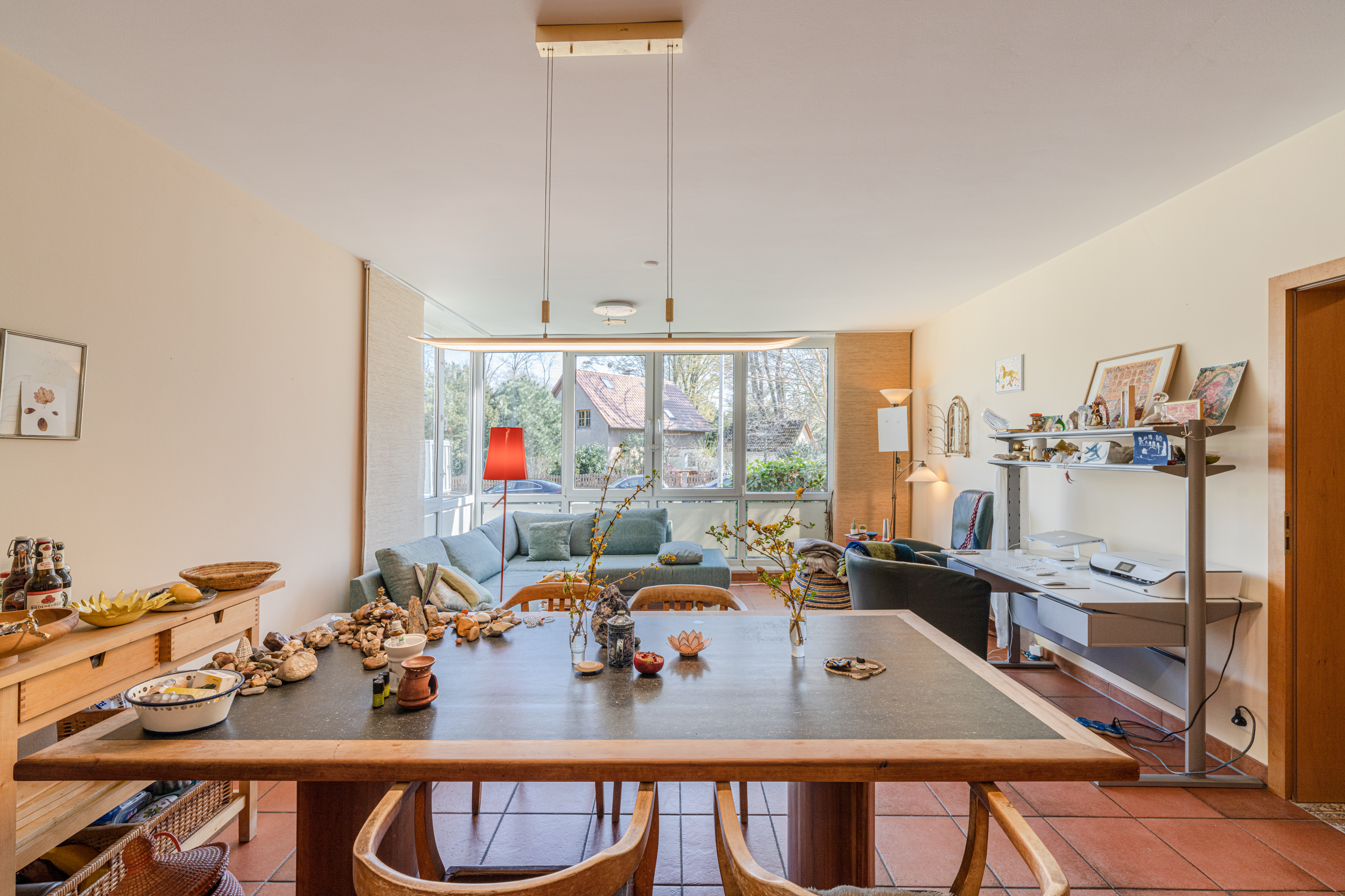 Helles Wohnzimmer mit Esstisch, Sofa, Schreibtisch und großen Fenstern mit Gartenblick.