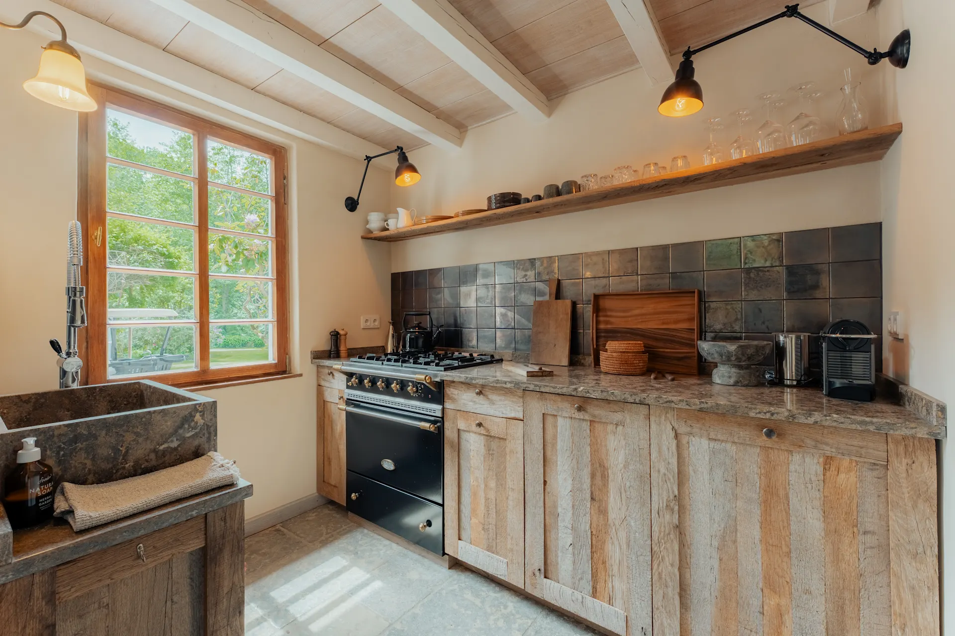 Helle Küche mit Holzmöbeln, großem Fenster und schwarzem Herd, offene Regale mit Geschirr.