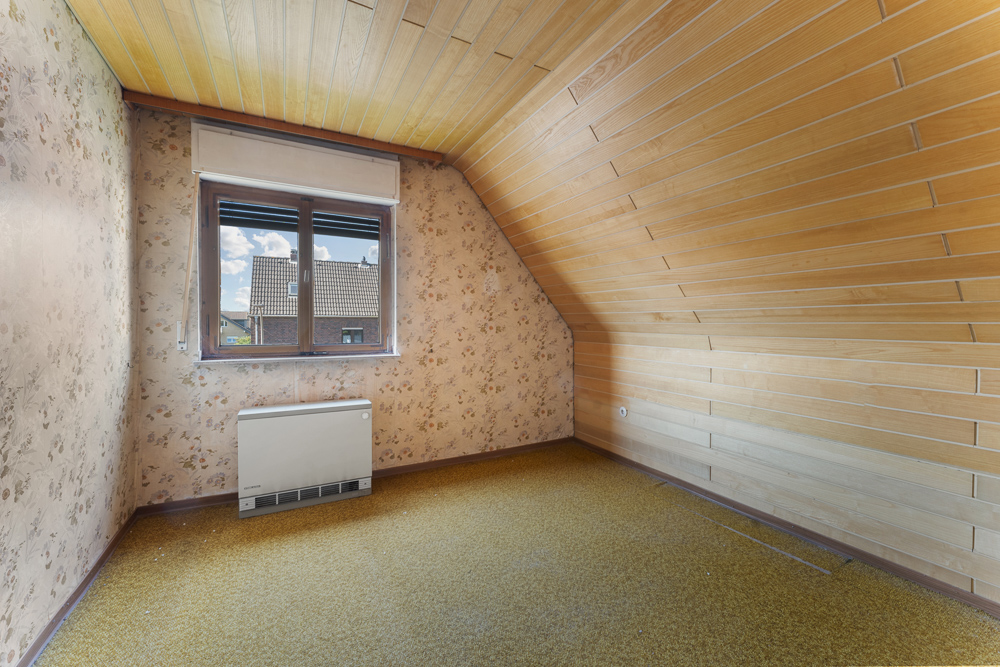 Kleines Zimmer mit gelbem Teppich, Holzdecke, Tapeten und Fenster mit Blick nach draußen.