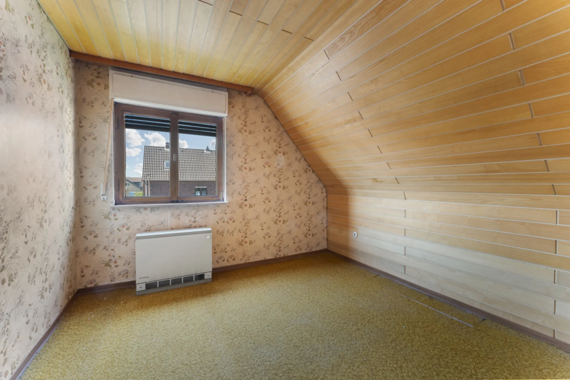 Kleines Zimmer mit gelbem Teppich, Holzdecke, Tapeten und Fenster mit Blick nach draußen.