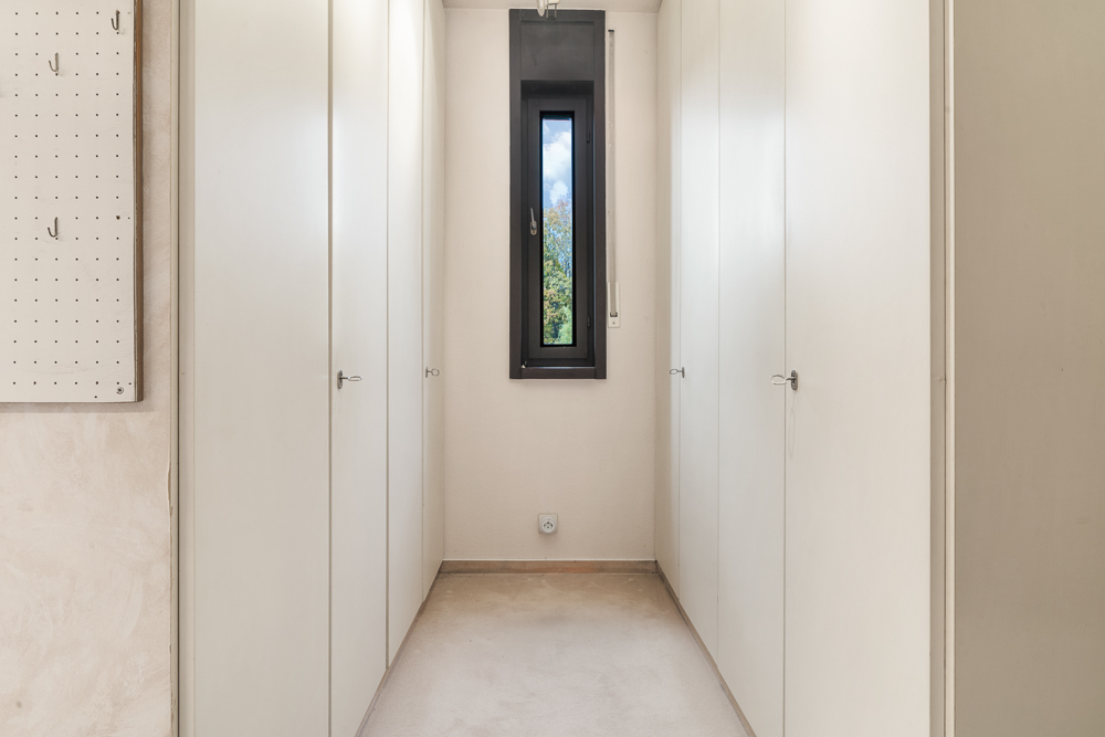 Heller Flur mit weißen Einbauschränken und kleinem Fenster am Ende.