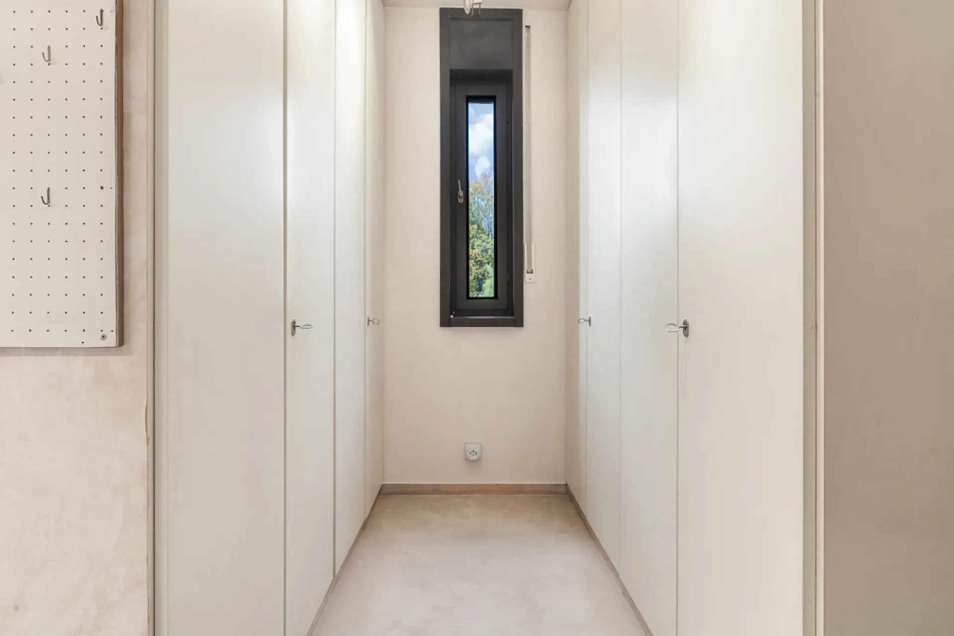 Heller Flur mit weißen Einbauschränken und kleinem Fenster am Ende.