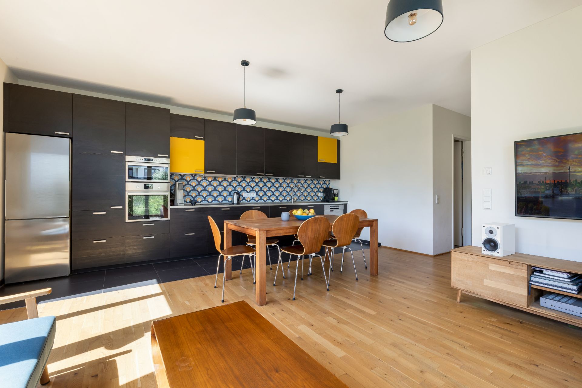 Moderne offene Küche mit Holz-Esstisch und sechs Stühlen in einem hellen Wohnraum.